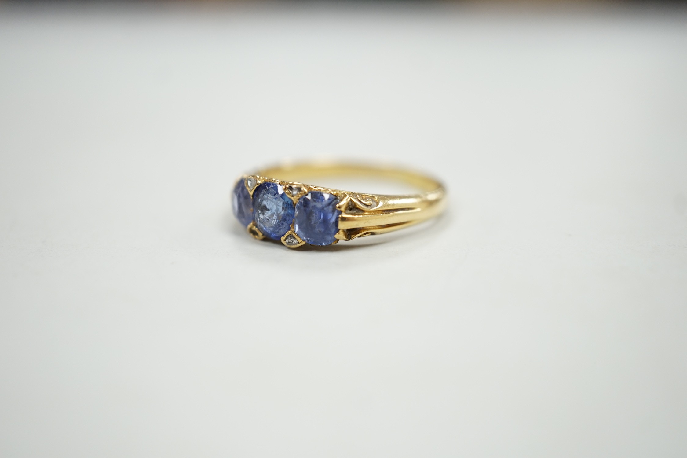 An early 20th century 18ct and three stone sapphire set half hoop ring, with diamond chip spacers, size Q, gross weight 4.2 grams.